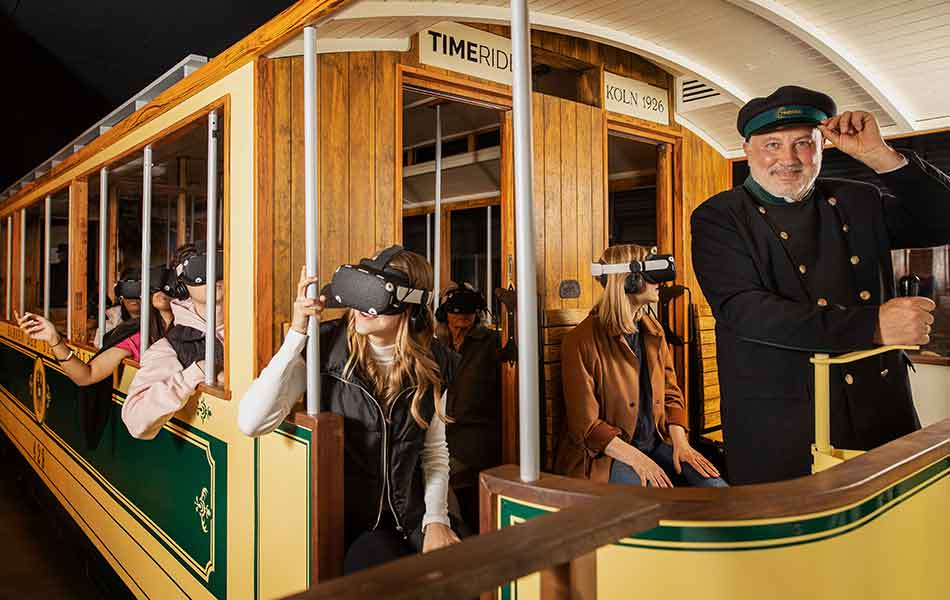 Fahrgäste mit VR-Brillen in historischer Straßenbahn, Schaffner tippt an Mütze, Senseum Köln