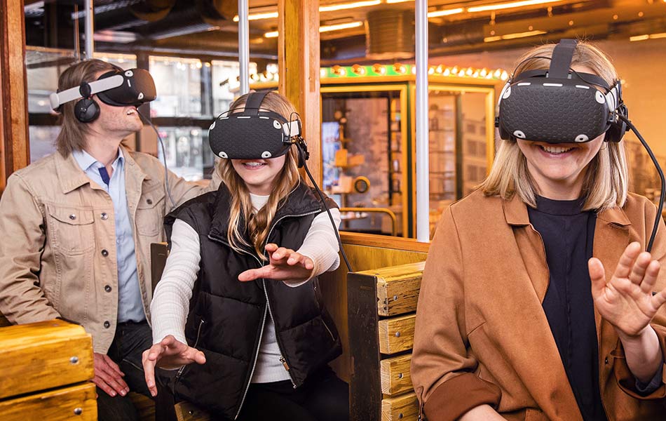 Drei Personen sitzen in einem Wagon und haben VR-Brillen auf